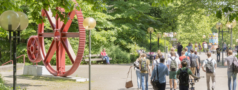 Students walk across the campus north. A large red sculpture in the shape of large gears can be seen.